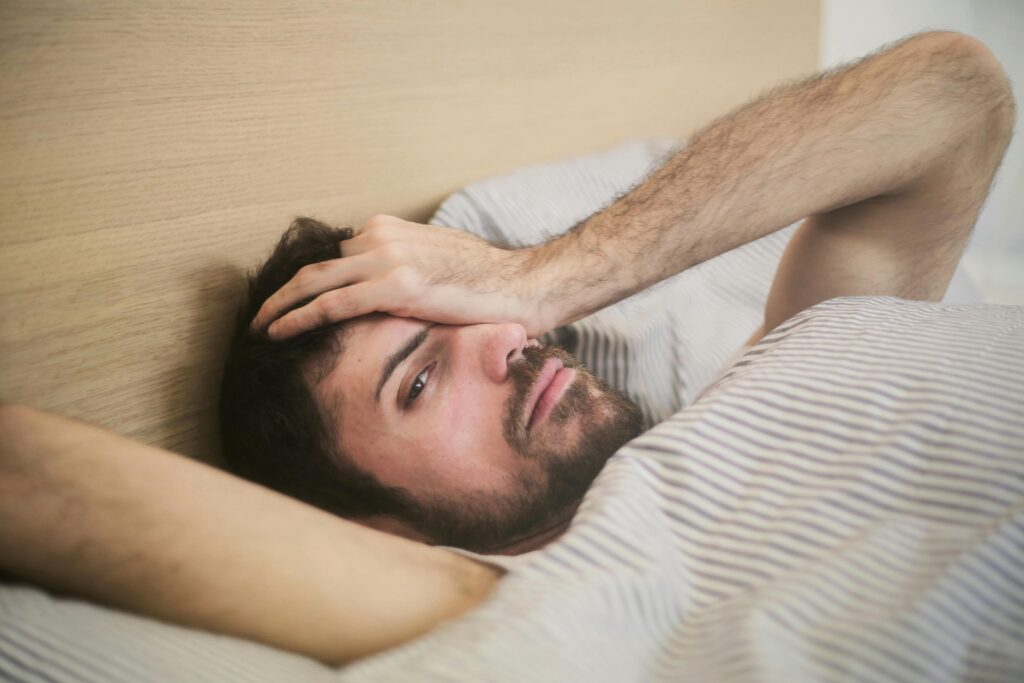 From above of sleepy bearded man just awakened rubbing eyes while lying on bed at home